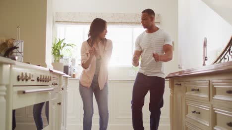 happy biracial couple dancing together and having fun in kitchen