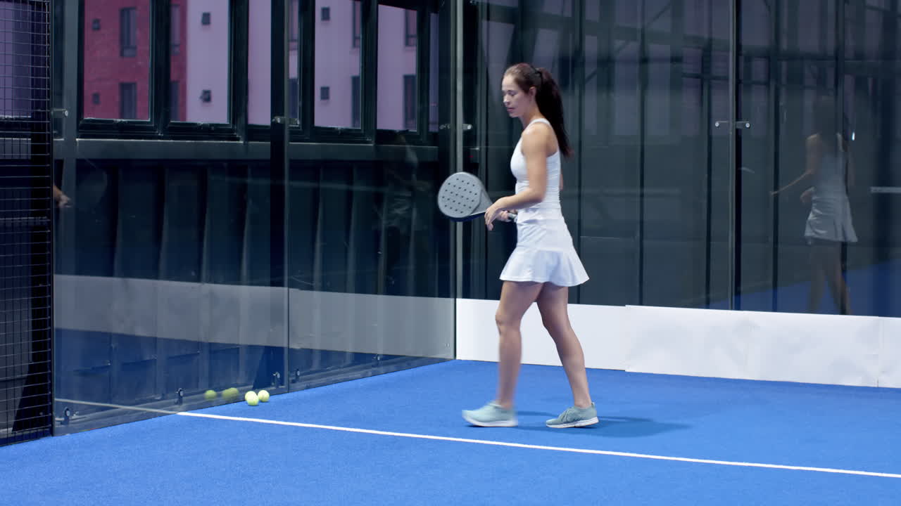 Woman playing padel tennis, focusing on hitting ball in indoor court, copy space