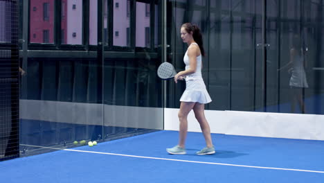 woman playing padel tennis, focusing on hitting ball in indoor court, copy space