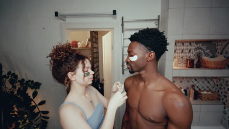 girl applying under-eye patches to face of boyfriend in bathroom