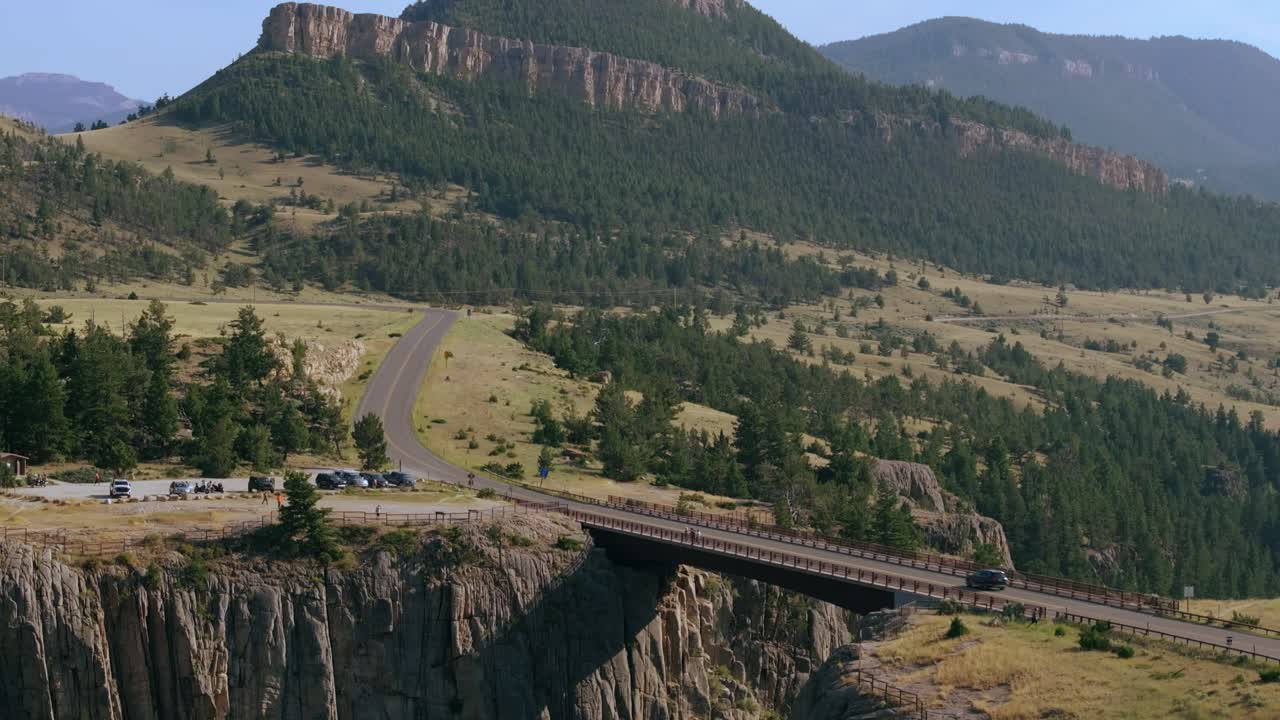 Aerial pullback tilts down across Sunlight Creek Bridge, Wyoming, showing the bridge's long span over the rugged canyon landscape