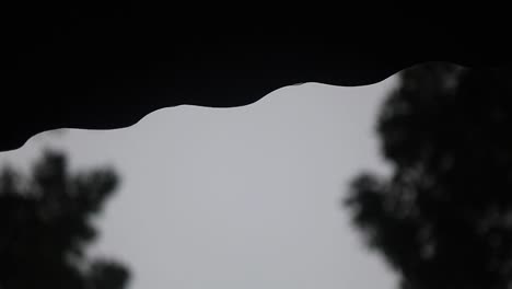 Raindrops-falling-from-rooftop-side-on-moody-day,-close-up-view