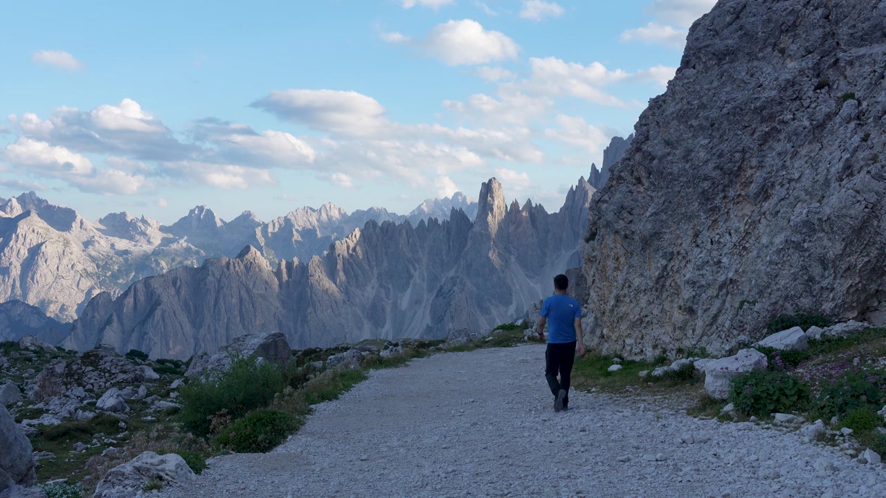 Filmato al rallentatore di un escursionista che cammina lungo il sentiero delle Tre Cime con le drammatiche vette dolomitiche sullo sfondo durante un pomeriggio estivo.