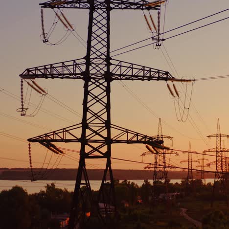 transmission lines near the river. high-voltage electric towers at sunset. distribution and supply of electricity. camera rising up.