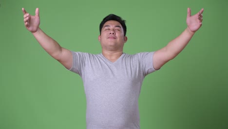 young handsome overweight asian man against green background