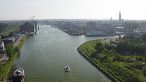 Aerial-shot-of-a-sailboat-sailing-on-the-Canal-through-Walcheren-towards-the-historical-town-of-Middelburg-in-Zeeland,-the-Netherlands,-on-a-sunny-summer-evening