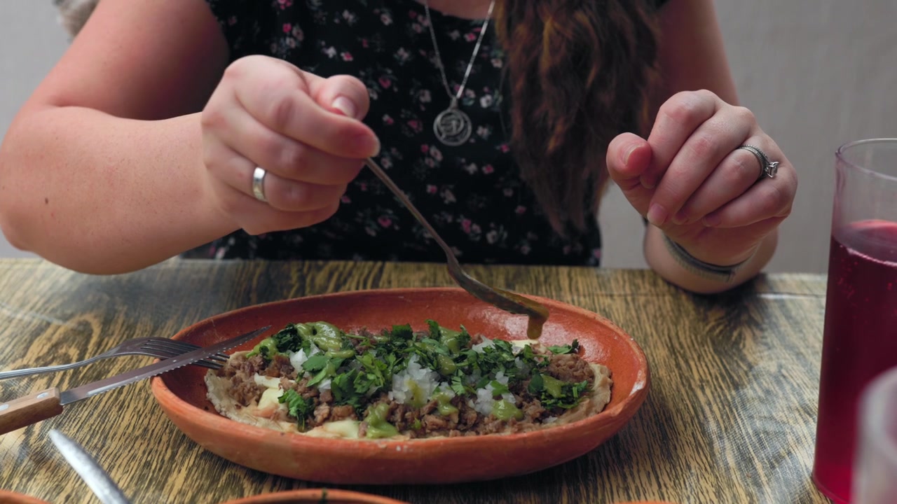 Kvinde hælder avocadogrøn salsa over traditionel mexicansk huarache toppet med kød, løg og koriander på et madmarked i Tapalpa, Jalisco, Mexico. Nærbillede.