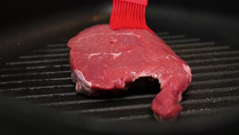 cerrar la toma en cámara lenta de un cepillo de cocina rojo cepillando un filete de ternera con aceite mientras se fríe en la cocina para una cena deliciosa