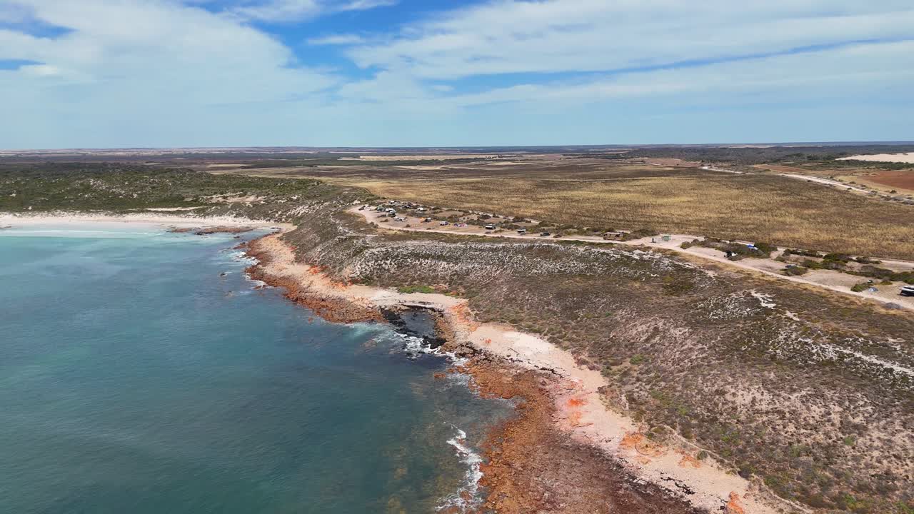 Recuo aéreo de falésias escarpadas e litoral rochoso que se estende até o oceano em Daly Head, campistas em terreno plano
