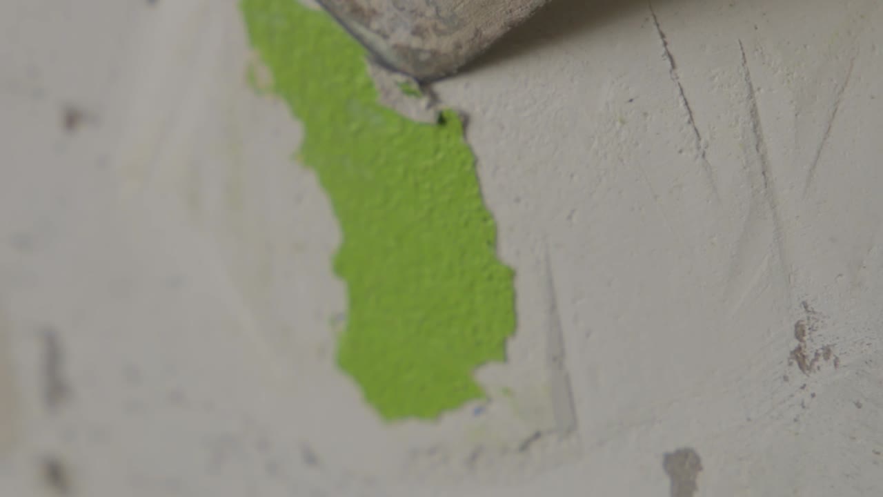 primer plano estable de un hombre que lucha por raspar la pintura verde de una pared