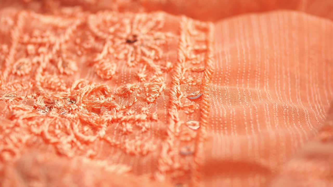Primo piano di tessuto ricamato color corallo con paillettes