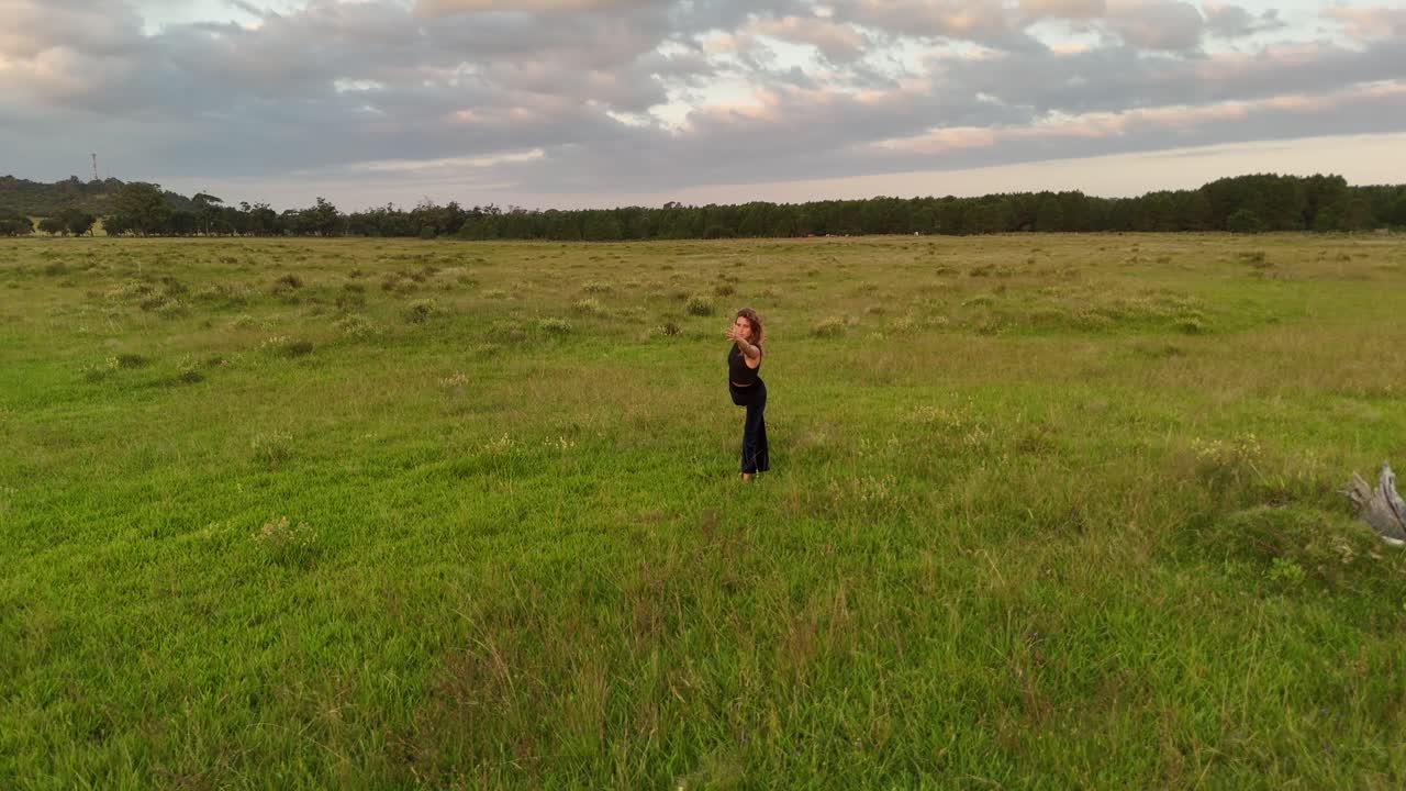 Aerial view of Woman making flow stretching yoga on the grass at sunset. Orbit shot, Uruguay, Punta del Diablo.