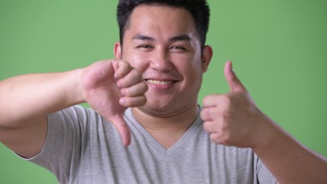 young handsome overweight asian man against green background