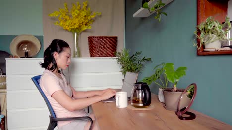 asian woman reading document on laptop and working at home