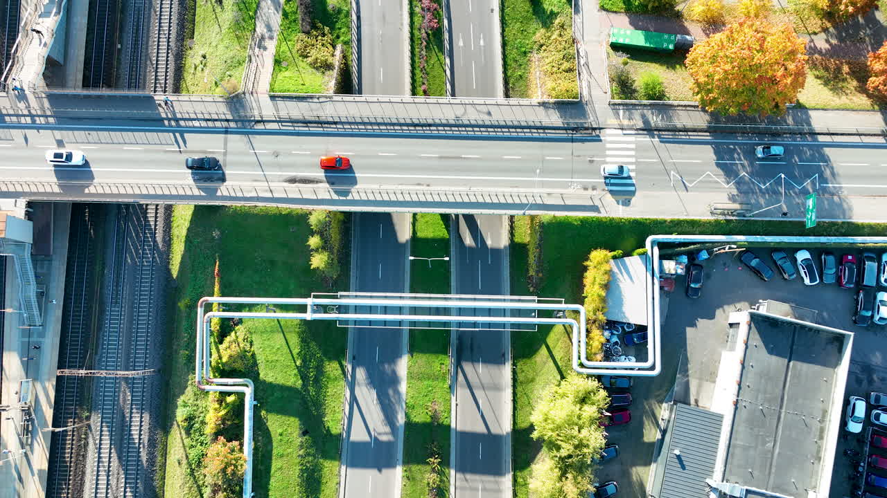Top-down drone view of road and railway infrastructure with pipelines and cars in motion