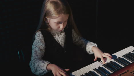 girl plays composition on synthesizer. small student executes musical piece in musical academy. early music education of child in audio recording studio