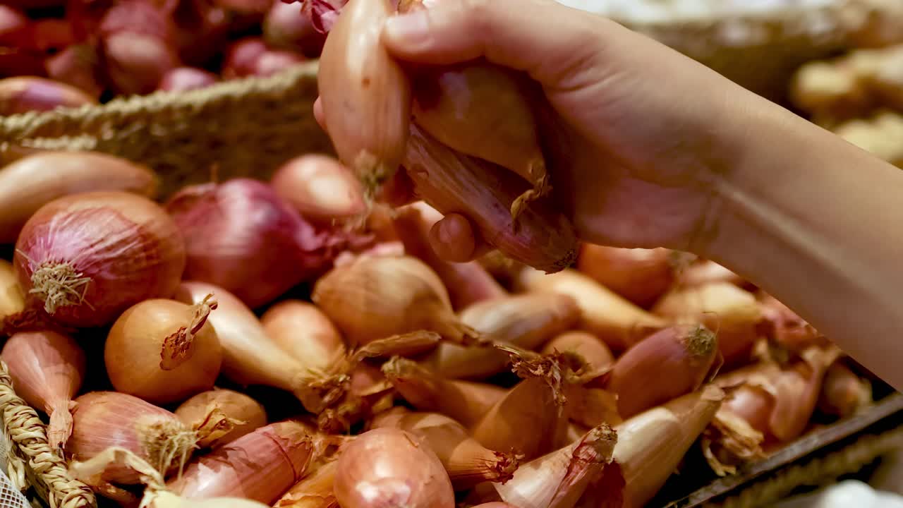 A hand carefully selects onions from a vibrant market display, showcasing a variety of colors and textures.