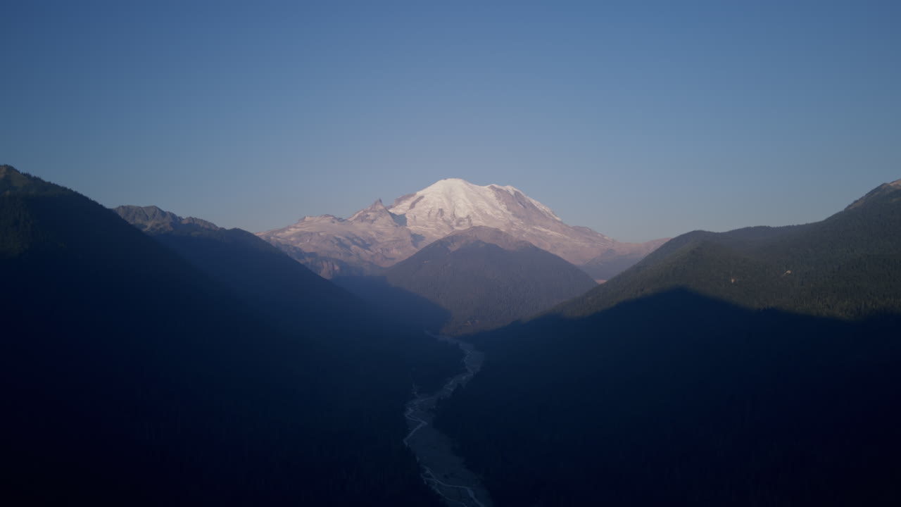 imágenes aéreas de las montañas alrededor del monte rainier con un valle con un río en el medio con una gran montaña cubierta de nieve en el fondo