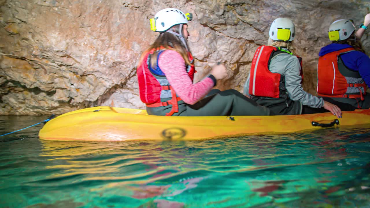 Tre donne caucasiche che viaggiano in kayak in un tunnel minerario sotterraneo con acque limpide, panoramica ravvicinata