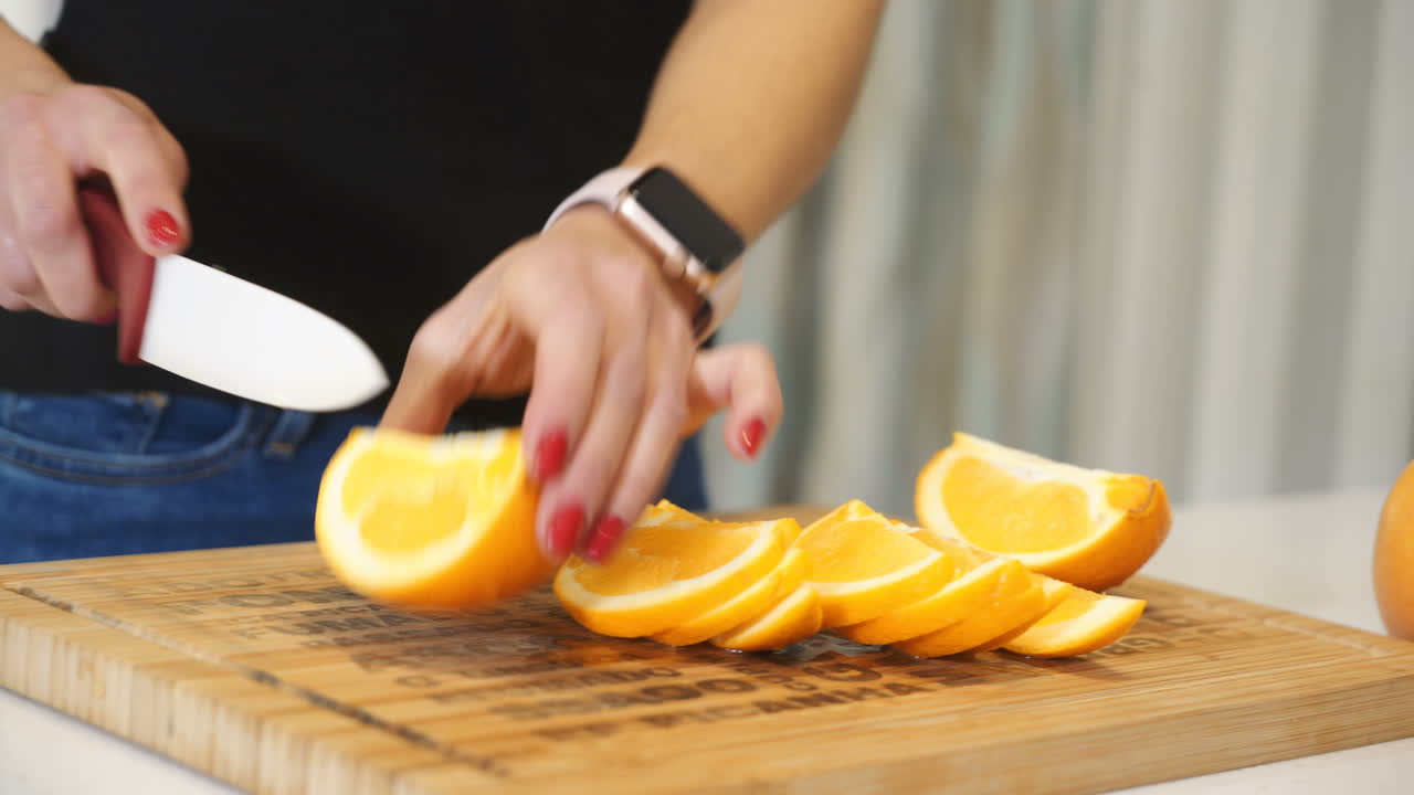 Female hands cutting orange on a wooden board. Woman in the kitchen. Healthy eating. Raw food.