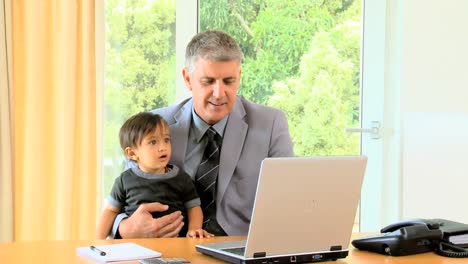 father in suit working on his laptop with child in his arms