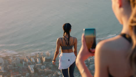 girl friends taking photo on mountain top using smartphone camera happy young influencer woman posing for friend with mobile phone sharing hiking adventure on social media