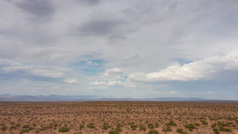 Slow-aerial-approach-towards-the-distant,-rugged-mountains-while-flying-over-the-Mojave-Desert's-barren-landscape