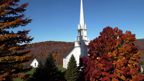 a beautiful white church steeple surrounded by vibrant autumn foliage against a clear blue sky