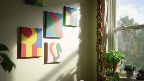 brightly colored abstract artwork displayed on a wall with sunlight streaming in, surrounded by various indoor plants and a cozy atmosphere