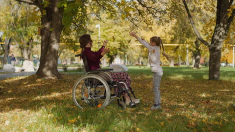 mother with legs injury and daughter play with autumn leaves