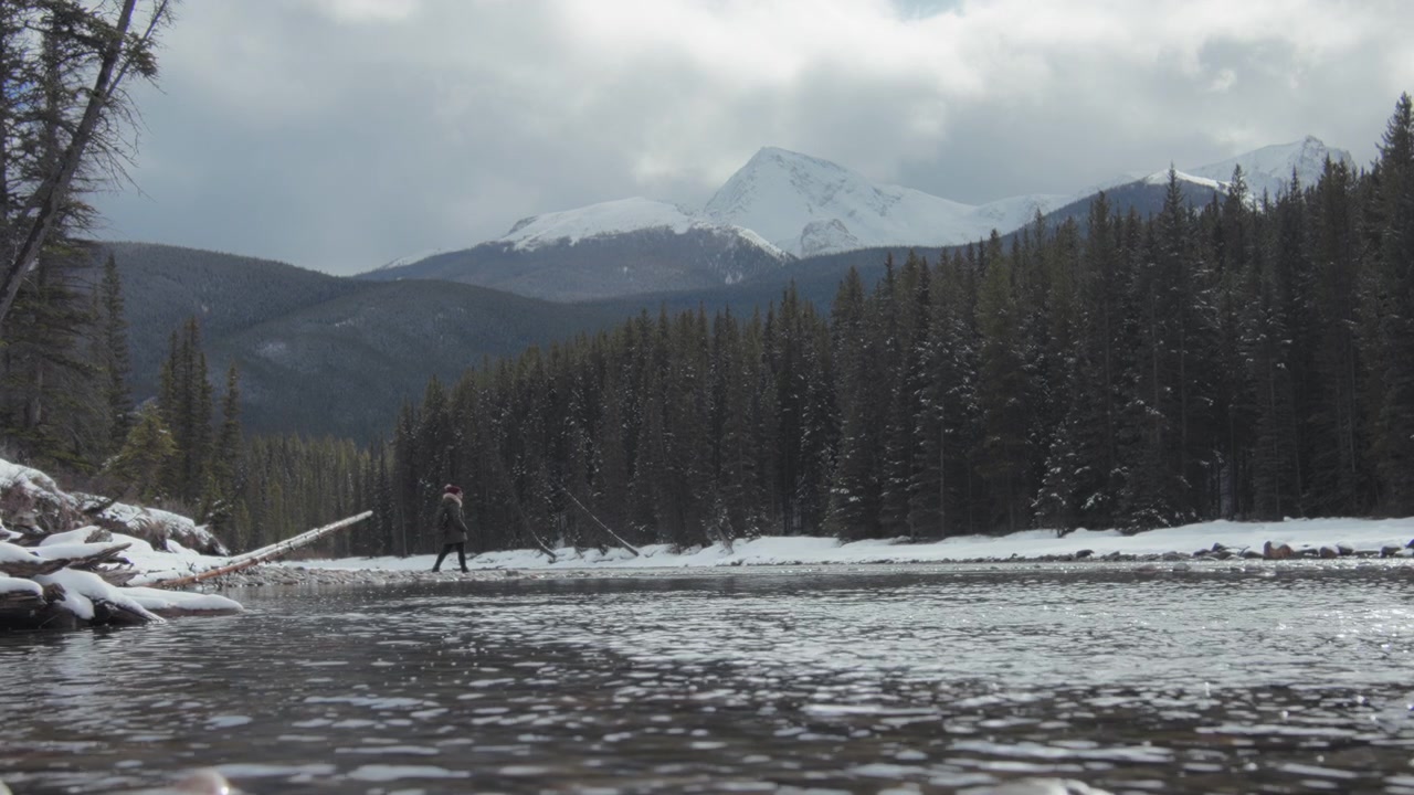 Escursionista che cammina lungo il fiume nelle Montagne Rocciose Canadesi in inverno