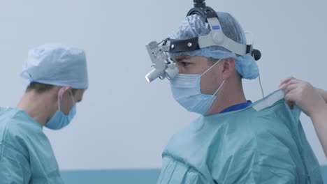 the surgeon prepares for the operation, fastens the sterile gown in the modern operating room. doctor is equipped in mask, medical headlamp, surgical loupes