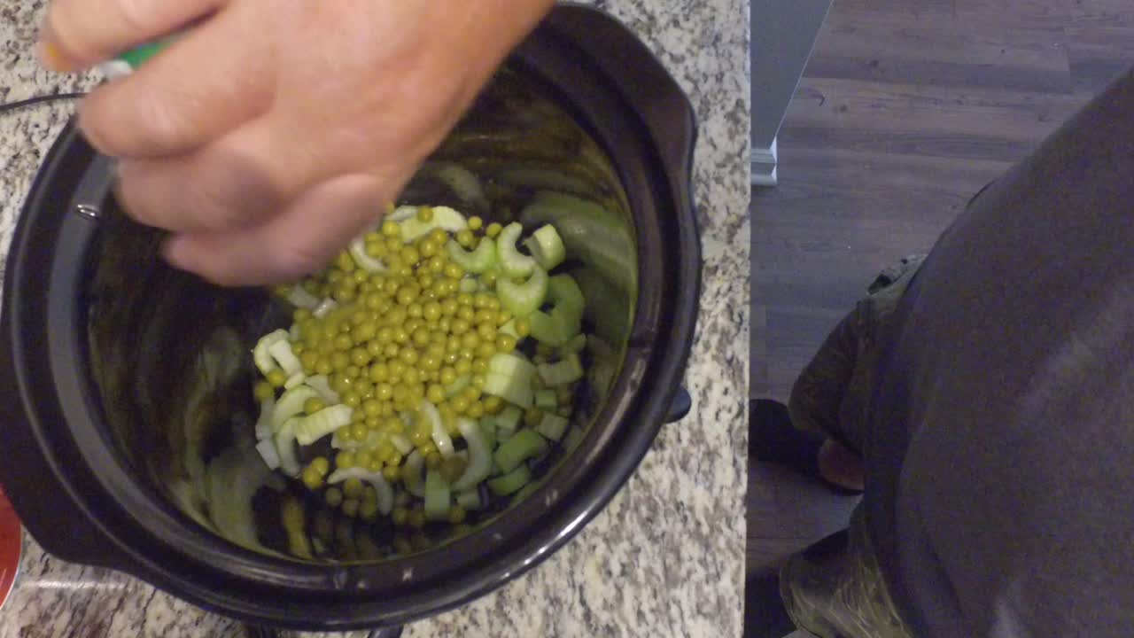 cocinar un guiso en una olla de cocción lenta mirando hacia abajo en la olla y revolviendo los guisantes, zanahorias y otros ingredientes