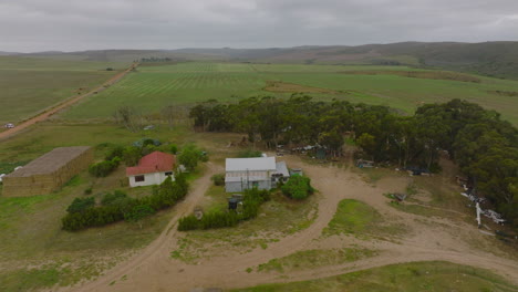 Vista-Aérea-De-Una-Pequeña-Granja-En-El-Campo-Africano.-Edificios-Y-Equipos-Rodeados-De-Campos-Verdes.-Sudáfrica