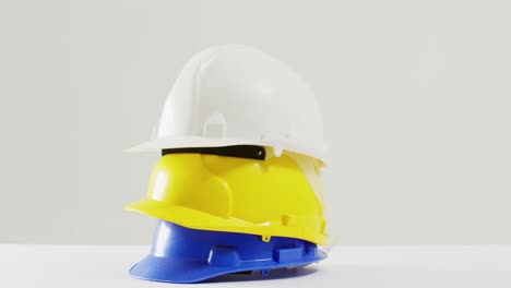 Video-of-close-up-of-colourful-building-helmets-on-white-background