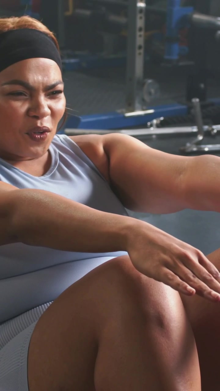 Vertical video: Performing woman in blue set sitting up at gym smartwatch tap starting core reps