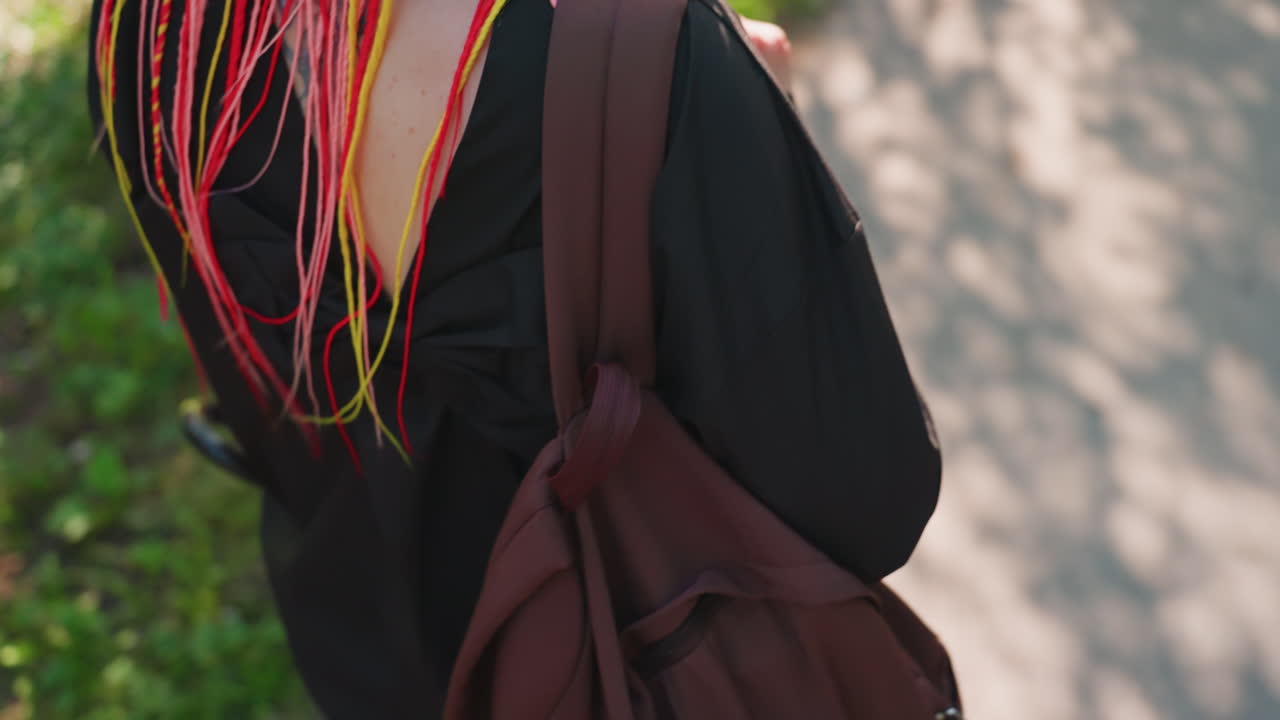 네온 브레이드 장식으로 치장한 여성이 거리를 걷고 있어요. 빛나는 다채로운 머리카락을 가진 여성을 강조하는 거리 풍경이며, 생생한 네온 색상의 땋은 머리와 도시의 그림자 연출로 여성의 모습을 담아낸 도시 배경입니다.