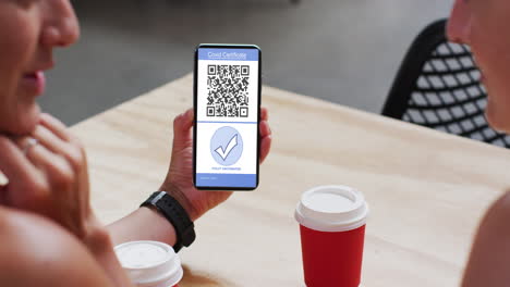 hombre en un café mostrando un teléfono inteligente con certificado de vacunación contra la covid y código qr en la pantalla