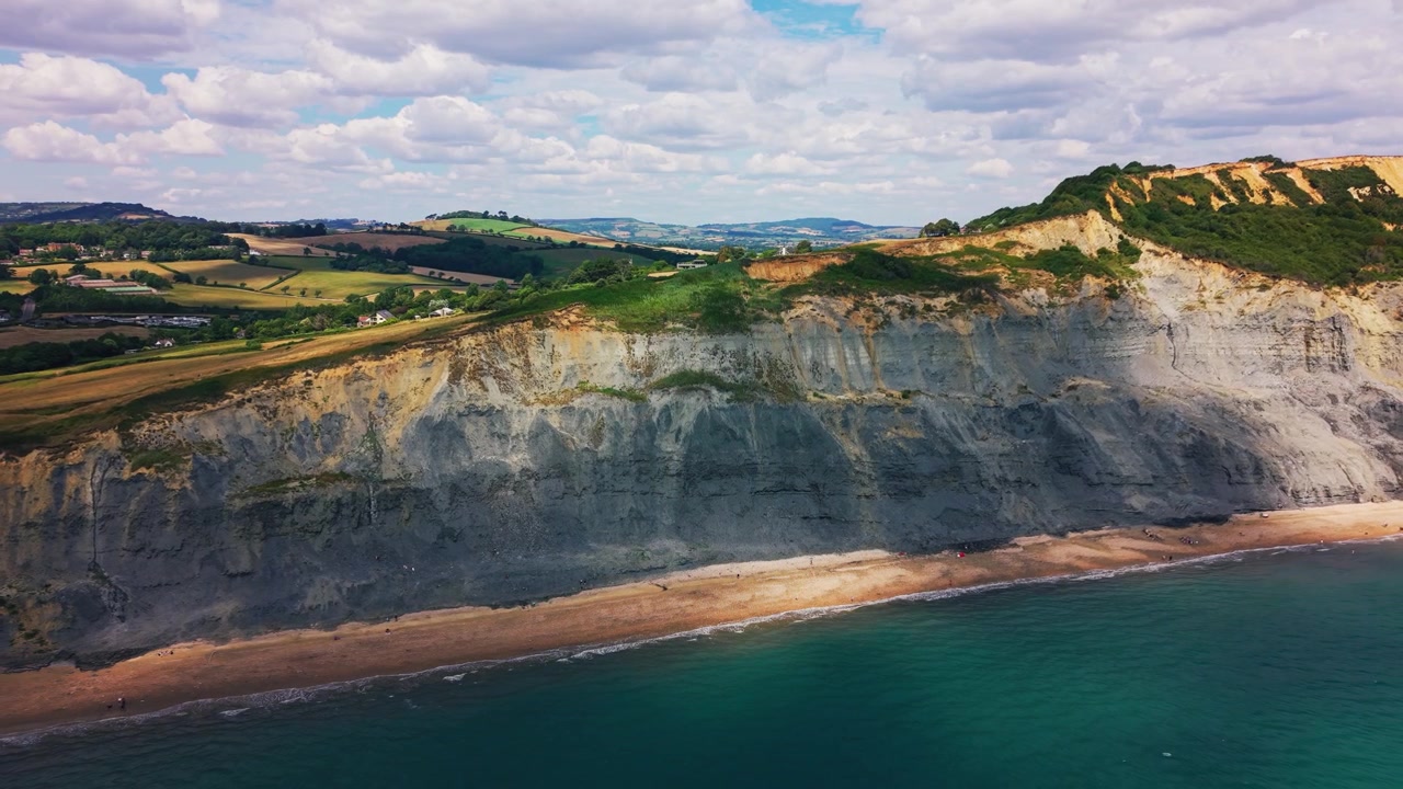 Dettagliate riprese aeree con drone che passano vicino alla scogliera esposta ed erosa a West Bay, sulla Jurassic Coast del Dorset, Inghilterra. Strati rocciosi visibili, sedimenti sciolti, vegetazione e modelli di erosione
