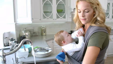 busy mother with baby in sling at home, slow motion