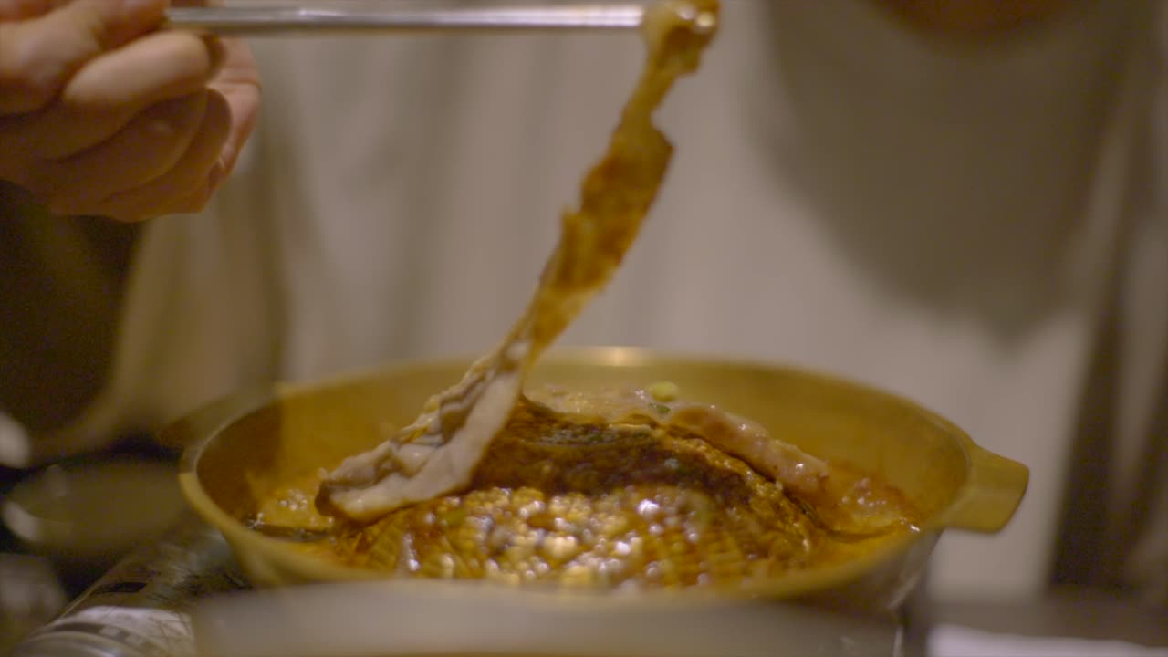 Sliced meat on Korean style hot plate grill flipped using chopsticks and cooked to perfection, filmed as slow motion close up shot