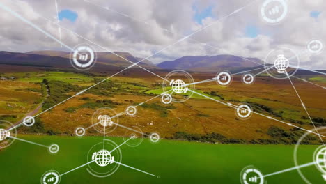 Animation-of-connected-icons-over-aerial-view-of-green-landscape-against-mountains-and-cloudy-sky