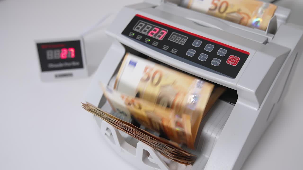 Hand puts a pack of fifty euro bills into money counting equipment. Machine for calculating currency at work close up. Blurred backdrop.