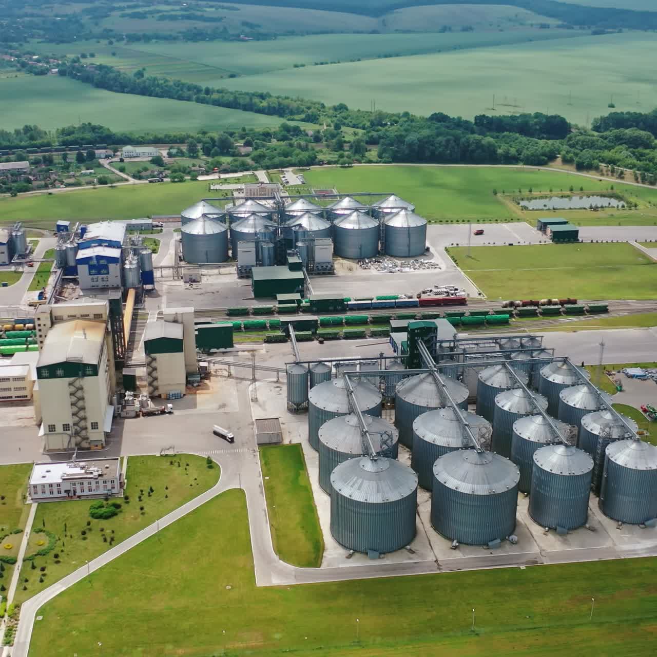 Large granary in a field. Industrial grain elevator on the background of green landscape. Elevator for storing agricultural products. Aerial view.