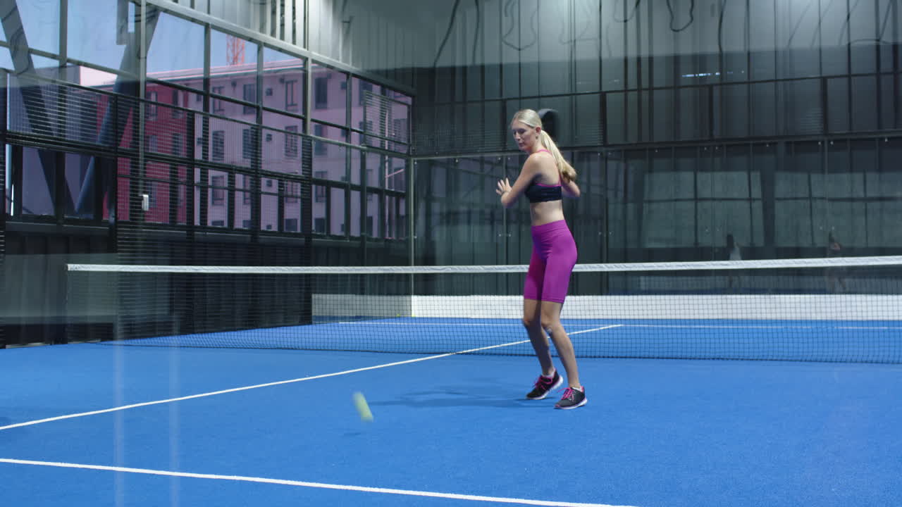 Woman playing padel tennis, hitting ball with racket on indoor court