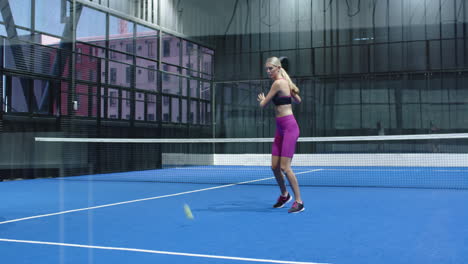 woman playing padel tennis, hitting ball with racket on indoor court
