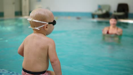 Junge-Mutter-Zeigt-Ihrem-Kleinen-Sohn,-Wie-Er-Im-Schwimmbad-Unter-Wasser-Tauchen-Kann,-Während-Er-An-Der-Grenze-Sitzt