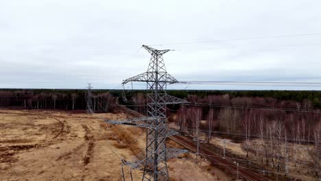 aerial view of a high-voltage power line pylon standing in a green field, under a clear blue sky, near railway