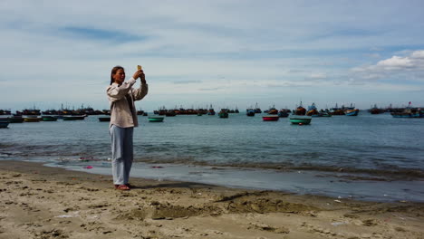 hermosa joven tomando selfies mientras está de pie en la playa de arena con montones de basura a poca distancia