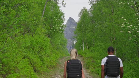 Couple-hiking-through-lush-forest-with-mountain-view-in-Norway